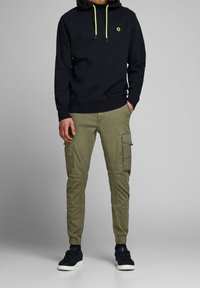Felpa navy con cordini gialli a contrasto, abbinata a pantaloni cargo khaki con tasche laterali e orli affusolati. Sneakers nere completano il look.