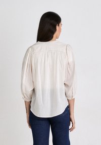 White and light pink striped blouse with puffed sleeves, rounded neckline, and gathered back detail, paired with dark blue jeans.