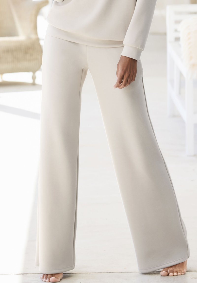 Helle beige weit geschnittene Hose aus weichem Stoff, mit einer glatten Textur und einem bequemen Bund, versehen mit seitlichen Schlitzen für mehr Bewegungsfreiheit.