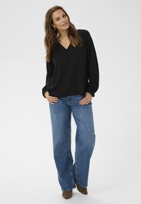 Top nero a maniche lunghe con scollo a V, abbinato a jeans a gamba larga blu chiaro e scarpe con tacco alto a stampa animale. Design semplice e casual.