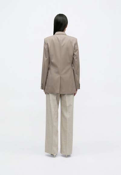 Ανοιχτό καφέ προσαρμοσμ�ένο σακάκι με καπάκι, συνδυασμένο με ανοιχτό μπεζ παντελόνι φαρδιάς γραμμής. Υφασμάτινη επιφάνεια, λεία φινίρισμα, μινιμαλιστικός σχεδιασμός.