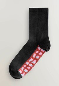 Schwarzer Socken mit gerippter Struktur, der einen bunten, gemusterten Bereich in Rot, Pink und Blau nahe dem Knöchel aufweist.
