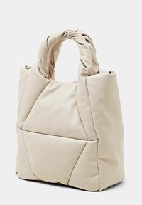 Beige taske i imiteret læder med et knyttet håndtag, polstret quiltet design og en struktureret krop med en forlomme.