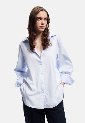 Lysblå bomulds skjorte med knapper, stor krave, lange ærmer og en afslappet pasform. Har en buet kant og diskrete knapdetaljer.