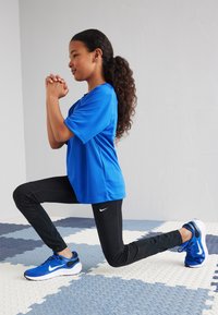 T-shirt de sport bleu, leggings noirs et baskets bleues. Le t-shirt est à manches courtes, et les leggings arborent un logo Nike sur le côté.