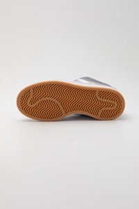 Suola della sneaker in gomma marrone con motivo a zigzag. La parte superiore presenta colori grigi e bianchi, materiali lisci e testurizzati.