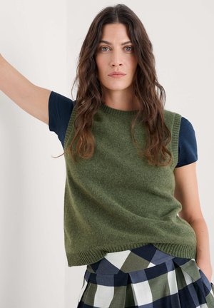 Green knit sleeveless sweater with a ribbed neckline, paired with a navy blue shirt and a plaid skirt in green and blue tones.