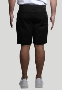 Pantaloni corti neri in cotone con orli risvoltati, dotati di tasche posteriori e taglio dritto. Indossati con scarpe sportive bianche.