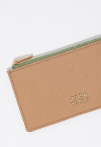 Cartera con cremallera en color marrón claro, textura suave, cremallera verde y logotipo en dorado "BIMBA Y LOLA" estampado en la parte frontal. Diseño contenido y compacto.