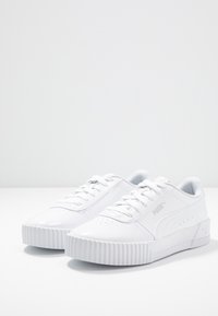 Baskets blanches, matériau synthétique lisse, design bas, bout rond, lacets plats, semelle rainurée, léger détail de marque sur le côté.