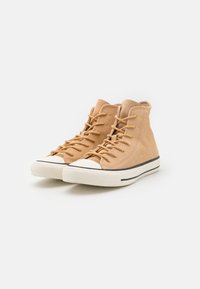Zapatillas altas de ante color marrón claro con punta y suela de goma blanca, con un diseño de cordones y una franja negra alrededor de la suela.