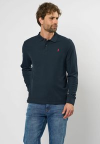 Marineblå langærmet polo-shirt med en subtil ribbet tekstur og en tre-knaps placket, der har et lille rødt logo på venstre bryst.