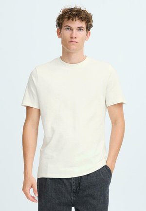 Kortärmad krämfärgad t-shirt i mjuk bomull, med rund halsringning och avslappnad passform, tillsammans med mörkgrå byxor.