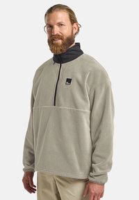 Light gray fleece pullover with a black high collar and quarter-zip. Features a chest pocket with a black logo patch. Soft texture.