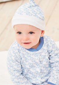 Kūdikių apranga pasižymi šviesiai m�ėlyno audinio, papuošto dramblio raštais, deriniu su balta skrybėle su šviesiai mėlynomis detalėmis.