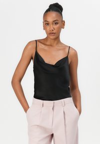Schwarzes Satin-Camisole mit dünnen Trägern, Wickelkragen und glatter Textur, kombiniert mit hellrosa, plissierten Hosen.