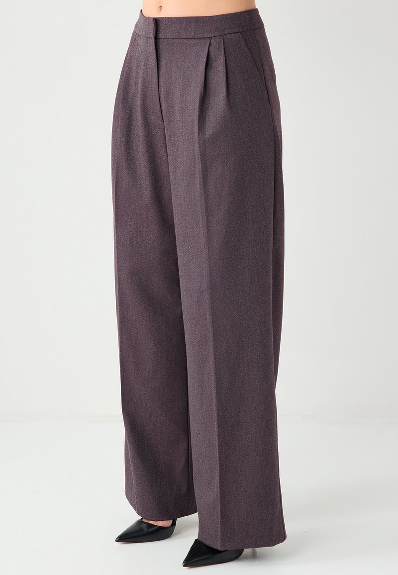 Pantalon à jambes larges en tissu texturé violet foncé. Présente des plis à l'avant et une taille haute, associé à des chaussures noires pointues.