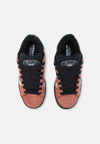 Sneakers with a mix of pinkish-brown suede and black accents, featuring black laces and a white logo on the tongue, low-profile design.