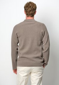 Pullovertröja i ljusbrun ribbad stickad tyg, med krage och långa ärmar, i kombination med ljusa byxor.