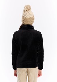 Zwarte fleecetrui met hoge kraag, zachte textuur en lange mouwen, gecombineerd met een beige gebreide beanie met een pompon bovenop.