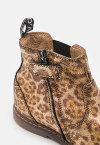 Bottines à imprimé léopard avec un éclat métallique, en cuir, côtés élastiques et fermeture à sangle. Détails de surpiqûre sur les coutures.