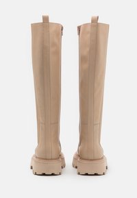 Polvisteiset beige nahkakengät, joissa on sileä pinta, jykevä pohja, takana vetoketju ja erottuva ommeltyö.