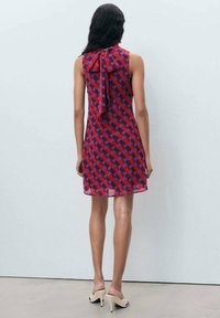 Rot und lila karierter Kleid mit einem Bindeband hinten, aus leichtem Material gefertigt. Ärmelloses Design, knielang, kombiniert mit neutralen Absatzschuhen.