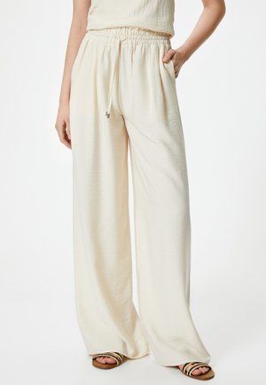 Weite cremefarbene Hosen aus strukturiertem Stoff, mit einem elastischen Bund und Zugkordel. Kombiniert mit Riemchensandalen.