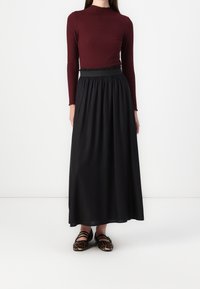 Jupe longue noire avec une taille froncée, associée à un haut côtelé bordeaux. Les chaussures présentent un motif léopard et un design à bandoulière.
