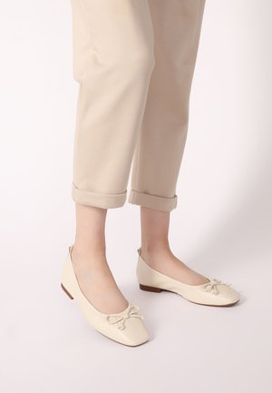 Ballet flats in beige leather with a square toe and decorative bow. Slender heel and smooth texture, paired with rolled cuff beige trousers.