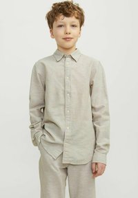 Camicia beige chiaro a maniche lunghe con bottoni sul davanti, colletto classico e tessuto morbido, abbinata a pantaloni coordinati per un look omogeneo.