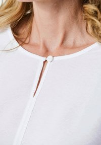 Top bianco con scollatura rotonda, piccola apertura a forma di chiave chiusa con un bottone bianco e una consistenza fine e liscia.