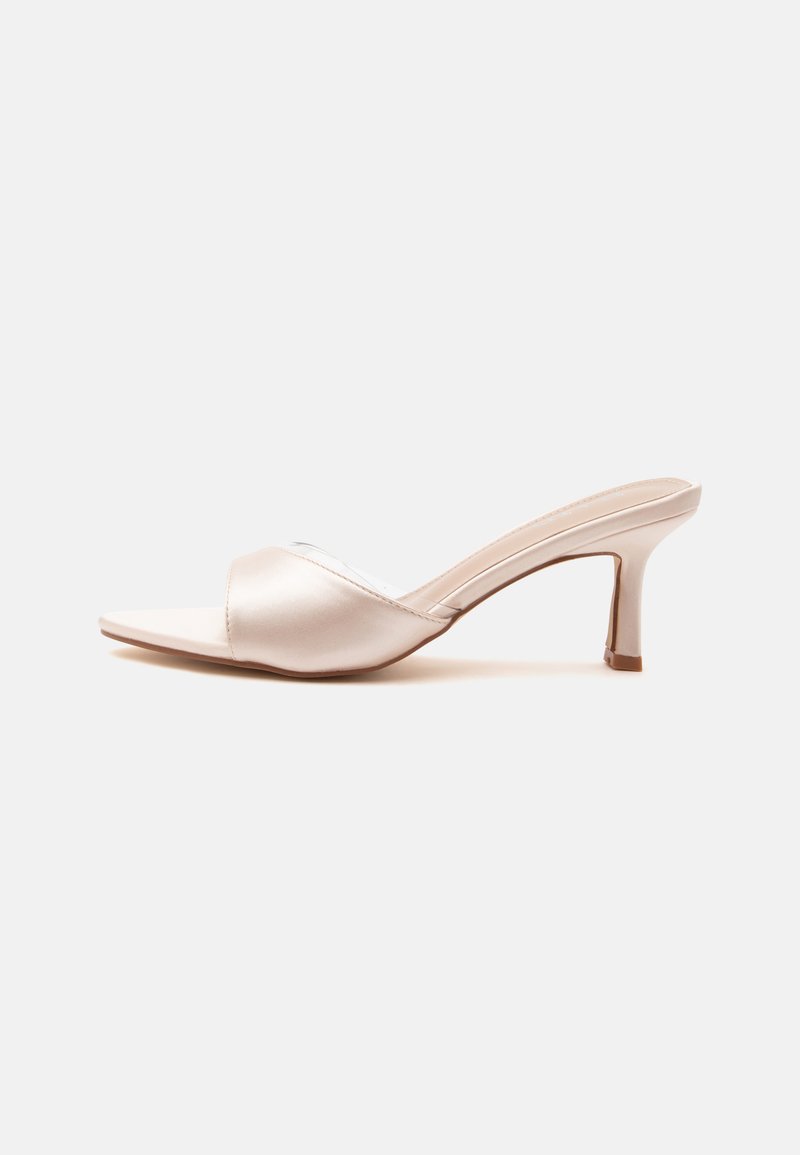 Mule beige à bout ouvert avec un talon fin de hauteur moyenne et une large bride lisse sur le dessus du pied.