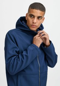 Sweat à capuche zippé bleu marine en tissu doux, avec un col haut, une fermeture zippée à l'avant et une capuche réglable. Texture lisse avec poches.
