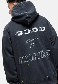 Zwarte oversized hoodie met de bedrukte tekst "GOOD For NOTHING" in het wit en met meerkleurige verfspetters, voorzien van een trekkoord bij de capuchon.
