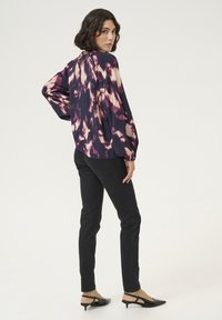 Dlhý rukáv, tmavo fialová blúzka s ružovým abstraktným vzorom, kombinovaná s čiernymi slim-fit džínsami a čiernymi topánkami na kitten podpätku. Hladká textúra.