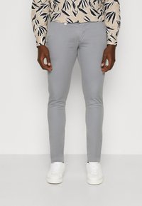 Light grey slim-fit pants with a smooth texture, featuring side pockets and a zipper closure, paired with white sneakers.