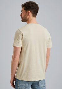 Kortærmet beige t-shirt lavet af blødt bomuld, med en klassisk rund hals og en afslappet pasform, båret sammen med lyseblå jeans.
