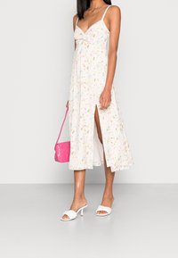 Vestido midi blanco con flores, tirantes finos, abertura lateral y un torso anudado; combinado con tacones abiertos blancos y un bolso rosa.