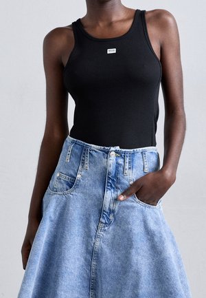 Femme portant un haut noir sans manches avec un petit logo et une jupe en denim bleu clair taille haute avec des poches.