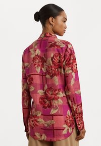 Floral button-up shirt with a pink and maroon rose pattern on a plaid background, featuring long sleeves and a slightly curved hem.