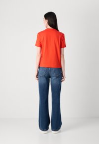 Rode katoenen t-shirt met korte mouwen, gecombineerd met hooggewaist flared denim jeans. De jeans hebben achterzakken en een klassieke blauwe wassing.