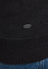 Zwarte gebreide trui met geribbelde zoom; bevat een klein, zilverkleurig ovaal logo-patch met de tekst "Petrol" op het lagere voorgebied.