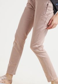 Ljust rosa, åtsittande byxor i mjuk bomull med sidfickor och en slät yta, i kombination med metalliskt rosa sneakers.