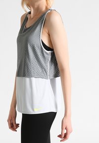 Mouwloze sporttanktop met een grijze mesh bovenkant met kleine gaatjes, een witte onderkant en een neongele Nike-logo aan de zoom.