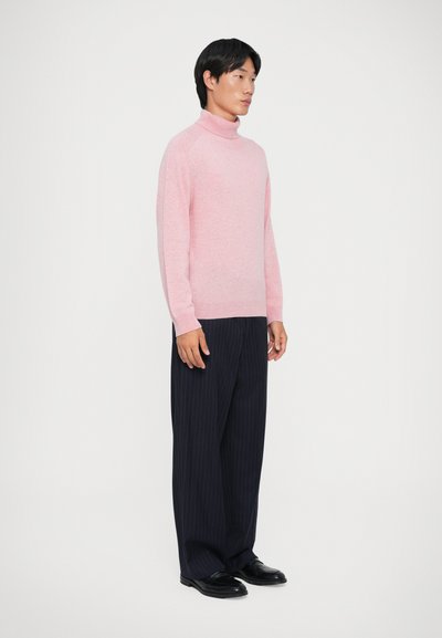 Jasnoróżowy sweter z golfem, z żeberkowym kołnierzem i mankietami, w połączeniu z ciemnogranatowymi spodniami w prążki. Gładka tekstura, luźny krój.