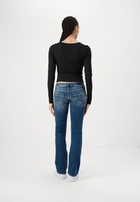 Black long-sleeve top, fitted design, paired with blue skinny jeans featuring rear pockets and subtle fading, worn with white sneakers.
