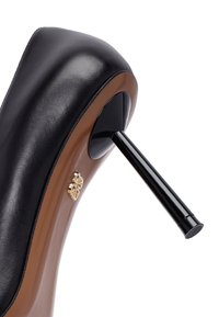 Scarpa nera in pelle lucida con tacco alto, dotata di una suola color tan e un accento dorato vicino al tacco. Il tacco a stiletto lucido nero contrasta con la parte superiore opaca.
