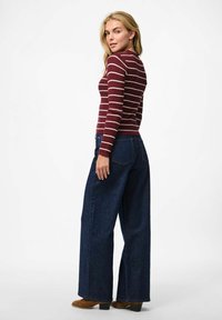 Bordeaux ribbel shirt met lange mouwen en witte strepen, gecombineerd met een wijd uitlopende donkerblauwe jeans en bruine haklaarzen.