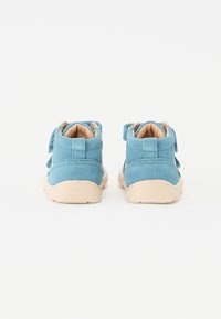 Botine albastre din suede cu talpă din cauciuc bej și curele cu arici. Prezintă cusături minime și un finisaj moale, texturat.